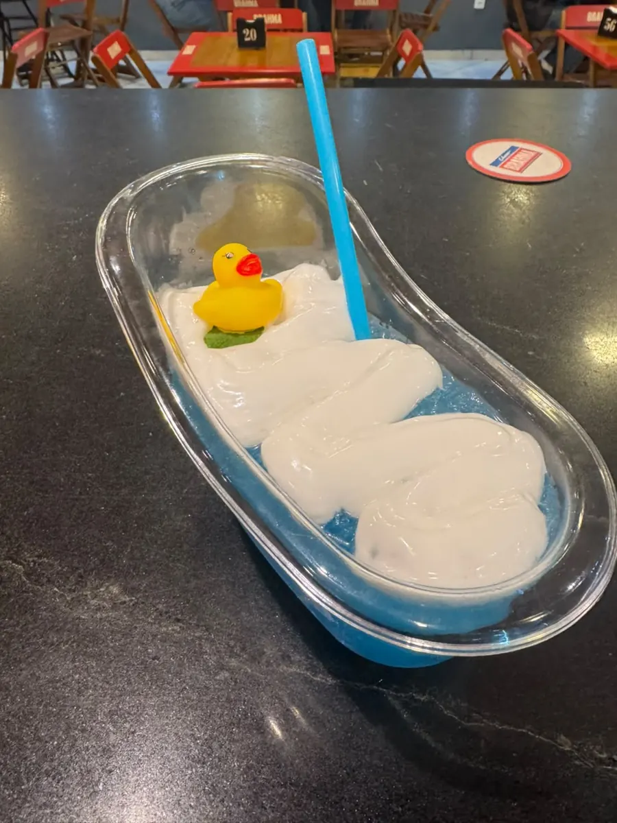 Drink azul servido numa banheira de vidro com espuma e patinho de borracha