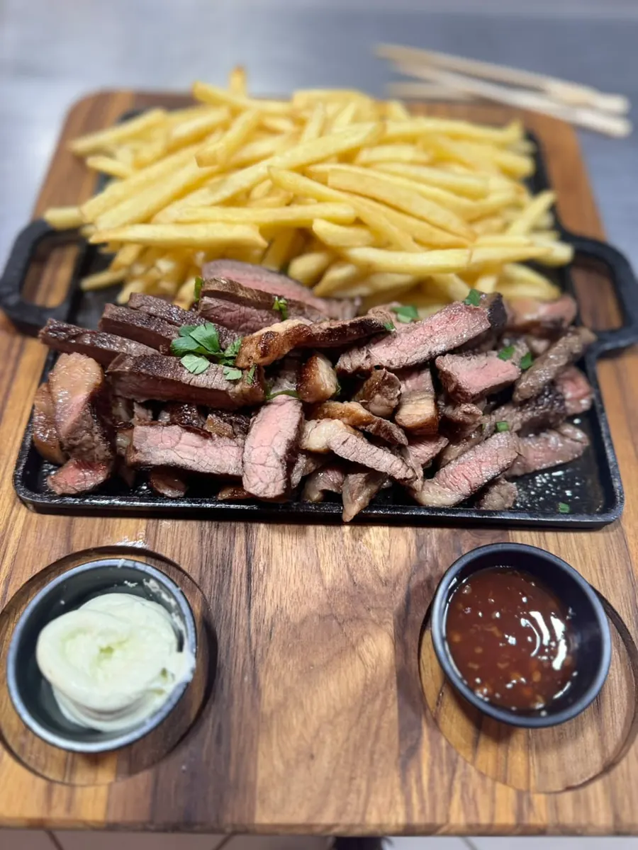 Porção de carne fatiada com fritas na chapa de ferro, com dois molhos